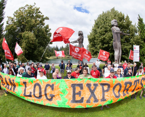 Ralliers hold a large sign reading "Ban Raw Log Exports" in Port Alberni