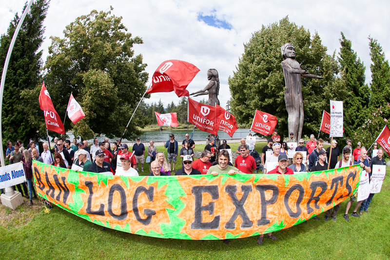 Ralliers hold a large sign reading "Ban Raw Log Exports" in Port Alberni