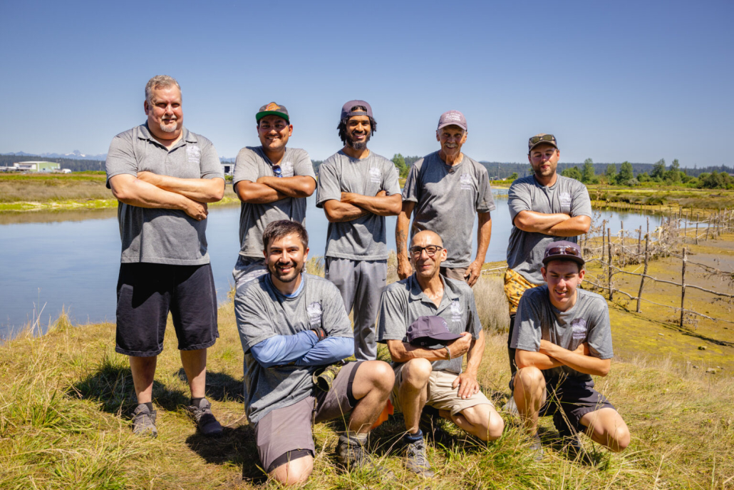 Members of the Wei Wai Kum Guardians, part of the Laich-Kwil-Tach group of First Nations stand together in a grassy field with a blue sky behind them.