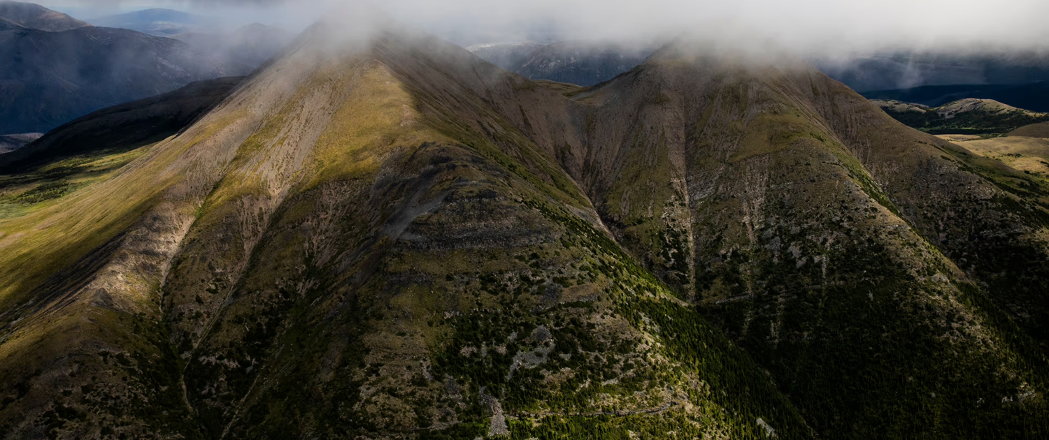 An aerial view of The Klinse-za (Twin Sisters) Mountains with grey, low hanging clouds hovering above them.