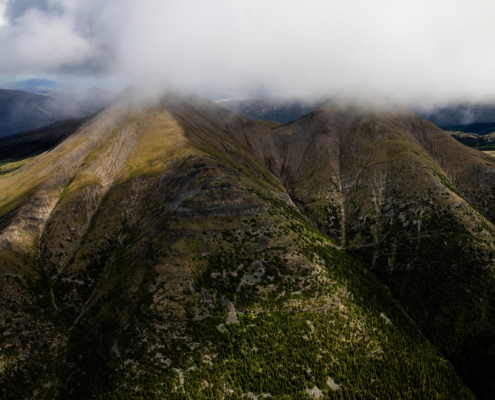 An aerial view of The Klinse-za (Twin Sisters) Mountains with grey, low hanging clouds hovering above them.
