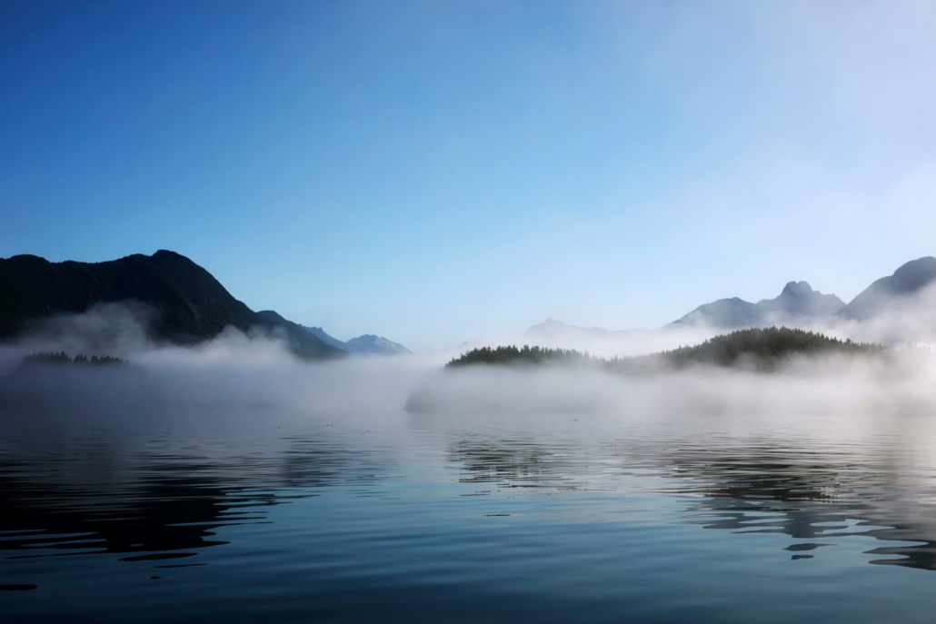 Morning mist hangs over Clayoquot Sound with mountains in the background.