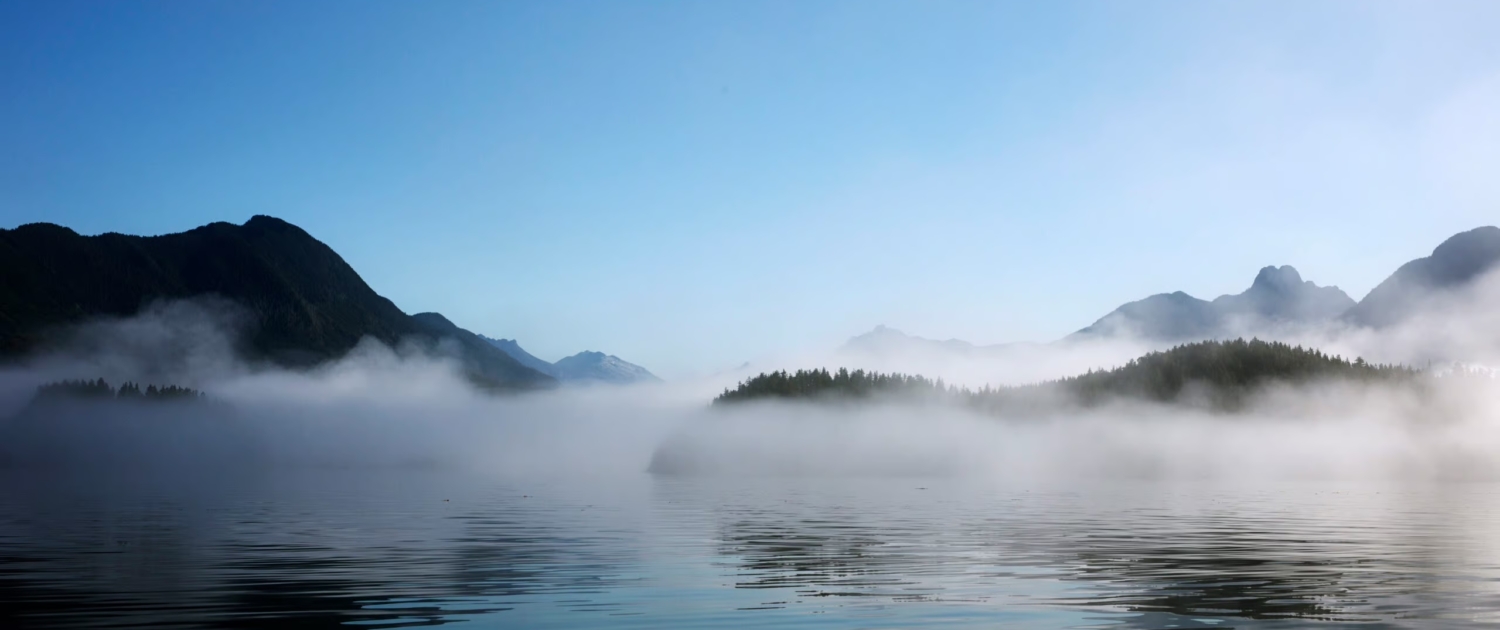 Morning mist hangs over Clayoquot Sound with mountains in the background.