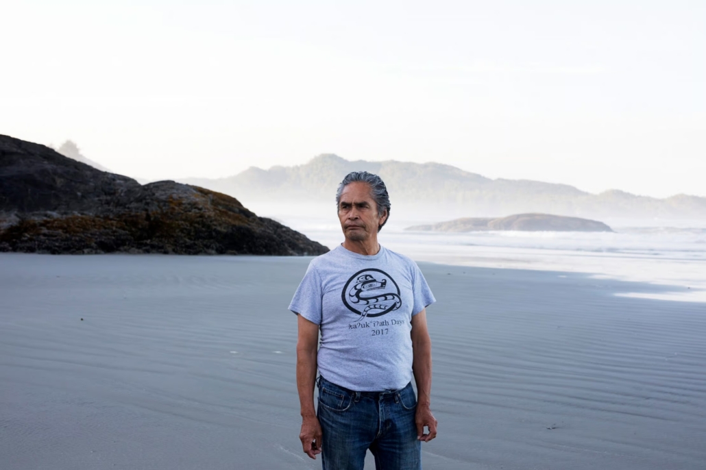 Master carver and Tla-o-qui-aht Elder Joe Martin stands on a sandy beach in Tla-o-qui-aht Territory.