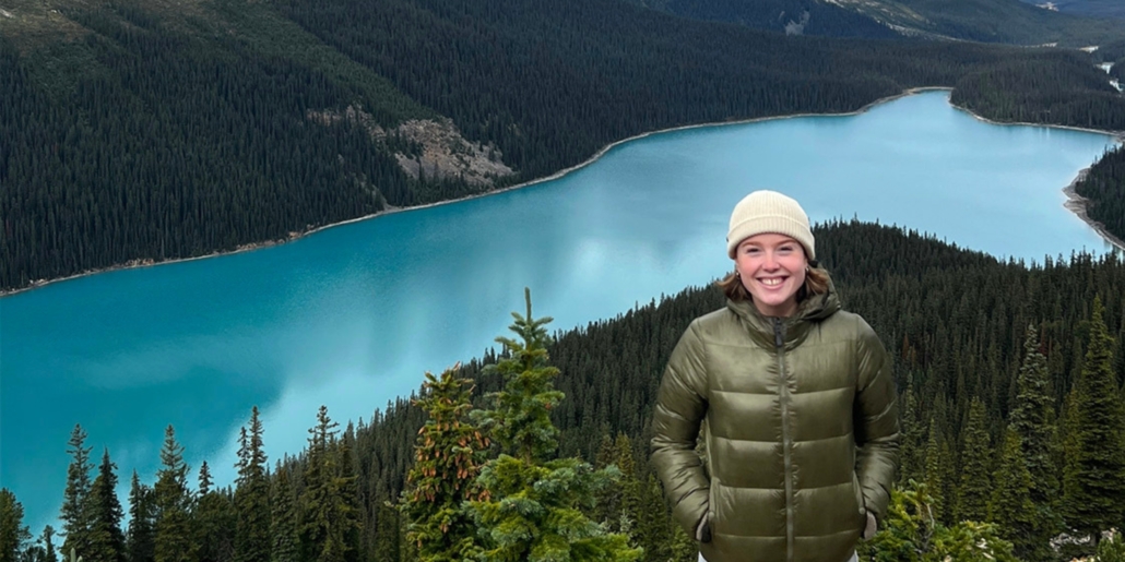 Issy stands on a mountain with Peyto Lake in the background behind her.