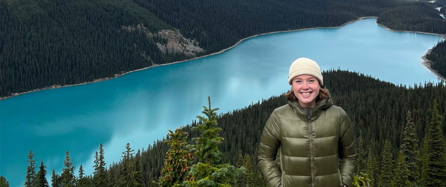 Issy stands on a mountain with Peyto Lake in the background behind her.